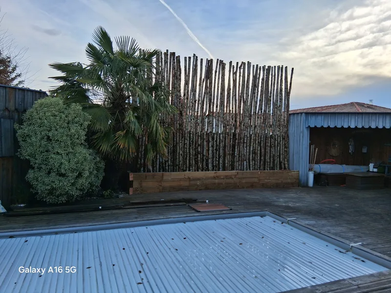 Vue large de la clôture en rondins avec terrasse bois et piscine au premier plan