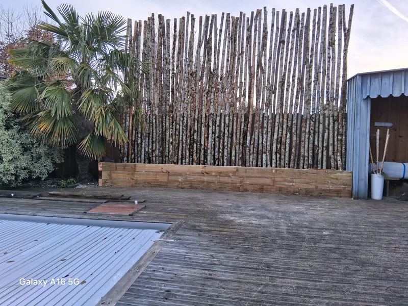Clôture en rondins de châtaignier verticaux avec bac de plantation et palmier