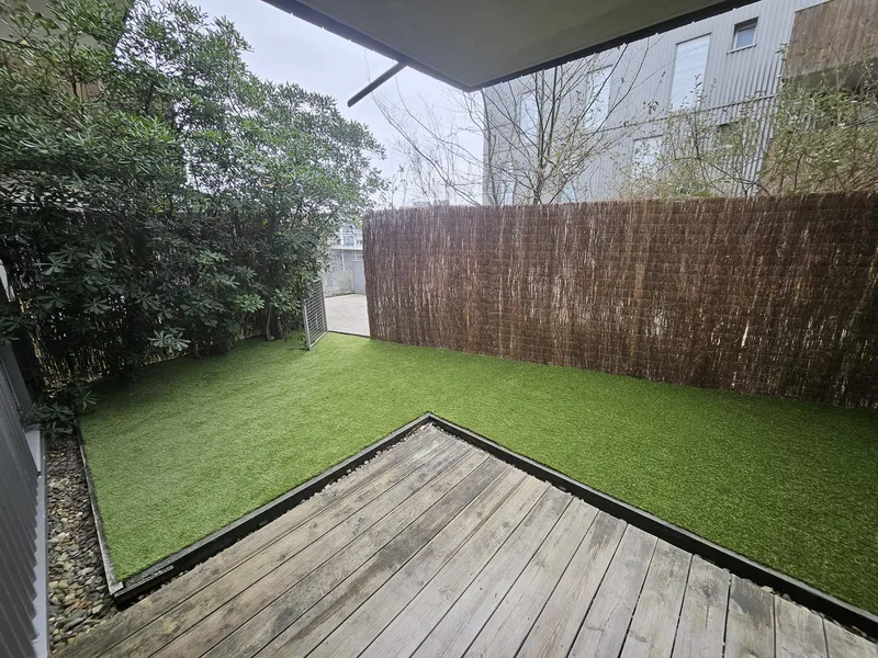 Cour avec gazon synthétique posé, brise-vue en bruyère et terrasse en bois